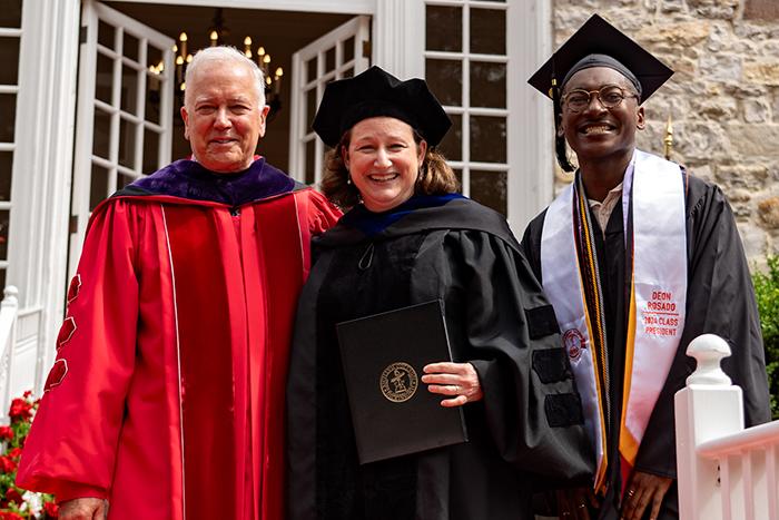 Photo of three people in academic regalia standing in front of a stone building.